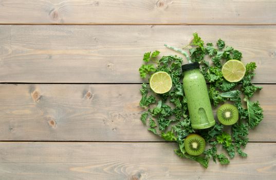 Green smoothie beverage in a bottle over a wooden table with ingredients