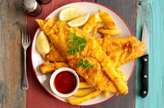 Close up of two pieces of battered fish on a plate with chips