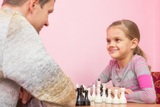 Dad and daughter happily look at each other, playing chess