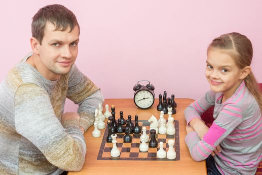 Dad and daughter playing chess with a smile and looked into the frame