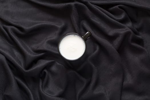 Cup of milk on the silk black fabric. Top view. Healthy diet. Clean eating. Tall glass with beverage. Breakfast, protein rich dairy product
