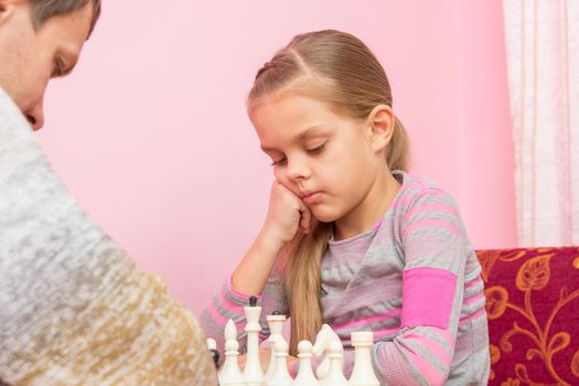 Seven-year daughter is thinking about the next move, playing chess