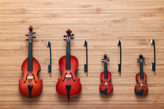 Set of four toy string musical orchestra instruments: violin, cello, contrabass, viola on a wooden background. String Quartet. Music concept. Cello and three violins, all vintage instruments.