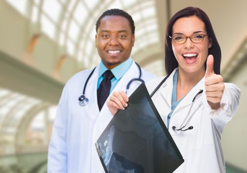 Female and Male Caucasian and African American Doctors in Hospital Office with X-Ray Film and Thumbs Up.