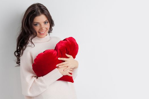 Beautiful woman in casual sweater holding red heart shaped pillow