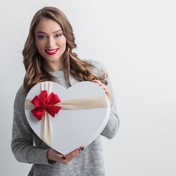 Young girl with heart-shaped gift box on white background