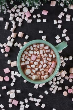 Hot chocolate in a green cup with marshmallows scattered around. Black background