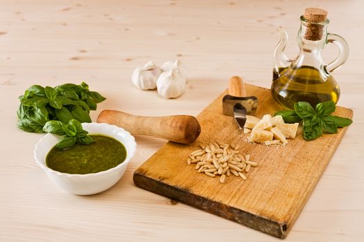 Fresh pesto genovese with its ingredients over a wooden background