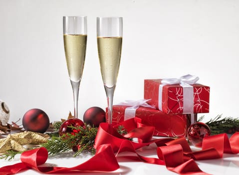 Two champagne glasses, christmas decoration and two red gifts with white ribbon