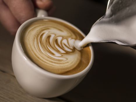 hand of barista making latte or cappuccino coffee pouring milk making latte art