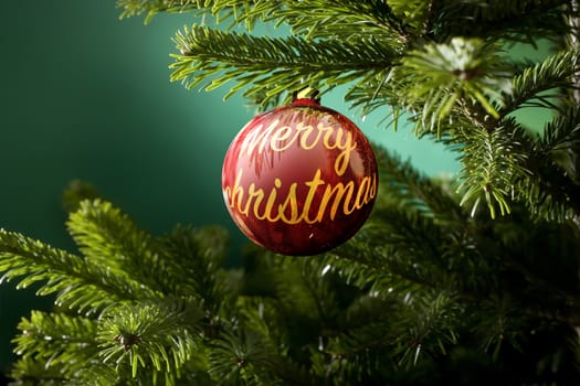 Christmas ball with the text merry christmas and green spruce branch on a green background
