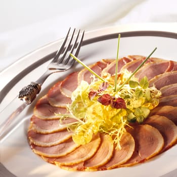 Duck ham with a green salade on white plate with a fork