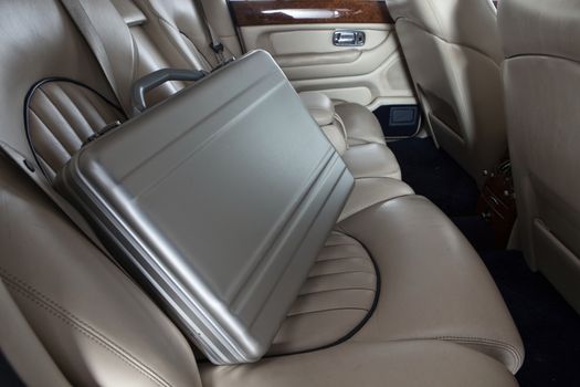 Luxury metal briefcase on the car back seat. Creme leather
