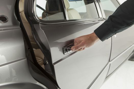 Middle aged businessman in classic suit is opening a car in a motor show, close-up
