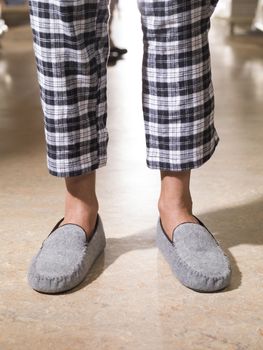 male feet wearing grey bedroom slippers on carpet.