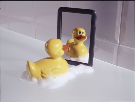 Plastic bath duck in soap foam before a mirror