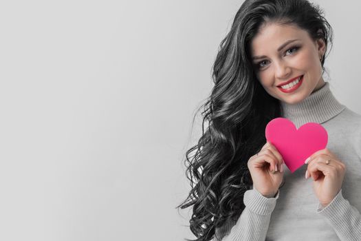 Beautiful young brunette woman holding pink paper heart, looking at camera