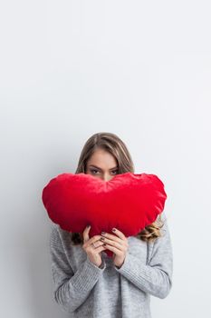 Beautiful woman in casual sweater holding red heart shaped pillow