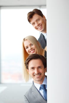 Happy business people looking out from corner in office