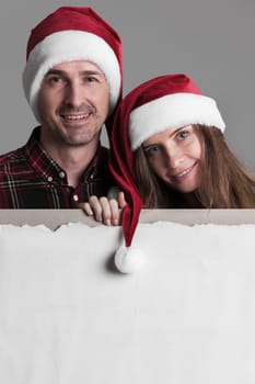 Happy smiling couple in Santa's hats with white blank banner with copy space