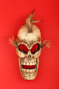 Handmade wooden carved creepy skull death joker mask on red background close up