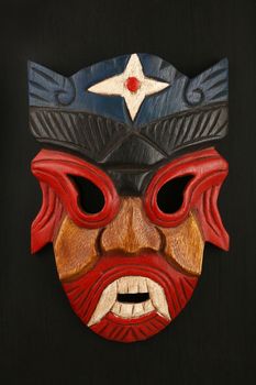 Asian traditional wooden red and blue painted mask with face of human or demon on black background