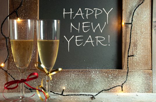 Two champagne glasses next to chalkboard with happy new year greeting