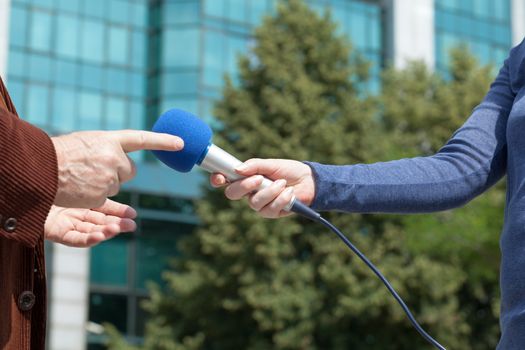 Female reporter holding microphone interviewing business person or politician