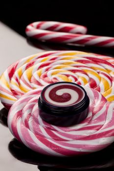 Cosmetic cream and lollipop on a glass studio background