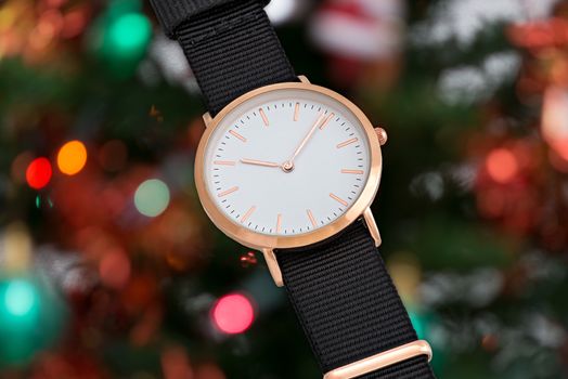 Wrist watch with black nylon strap in Christmas time in front of Christmas tree lights background