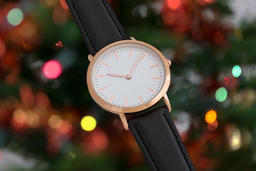 Black leather strap wrist watch in Christmas time in front of Christmas tree lights background