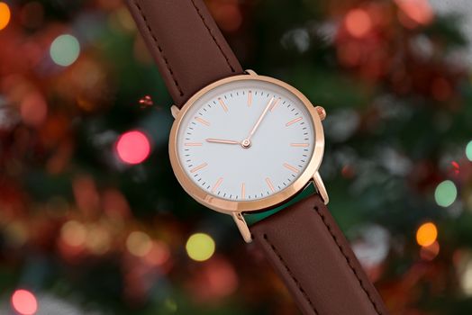 Brawn leather strap wrist watch in Christmas time in front of Christmas tree lights background