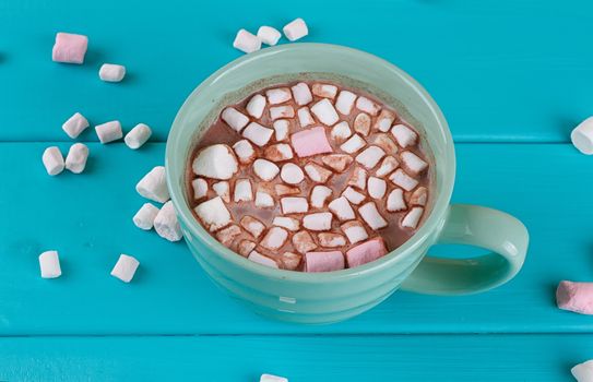 Blue cup of hot cocoa with marshmallows on blue wooden background
