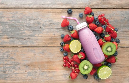 Berry smoothie in a bottle with ingredients on top of a wooden background with space