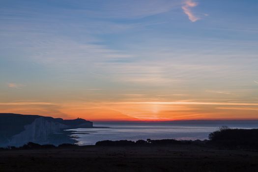 December sunrise from Seaford Head, looking South East over the English Channel with Belle Tout Lighthouse visible in the distance on the cliff-top.