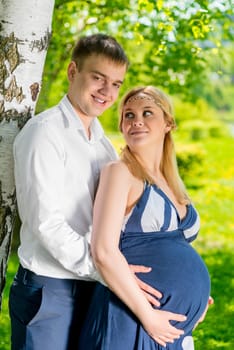 young family on a walk in the park, woman expecting a baby