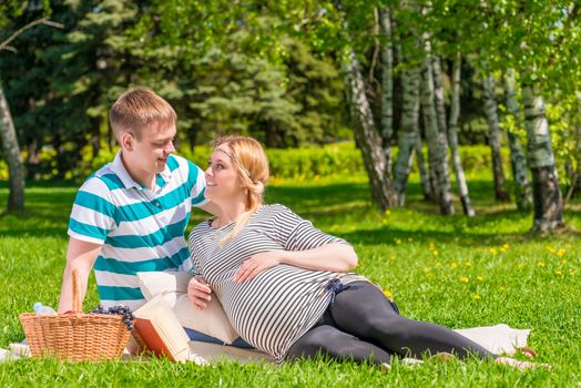 Pregnant couple resting on the plaid in the park