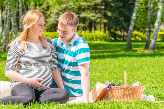 Young family resting in a park at a picnic, the girl with a big pregnant belly