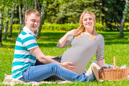 Beautiful young family having a picnic in the park, woman is pregnant