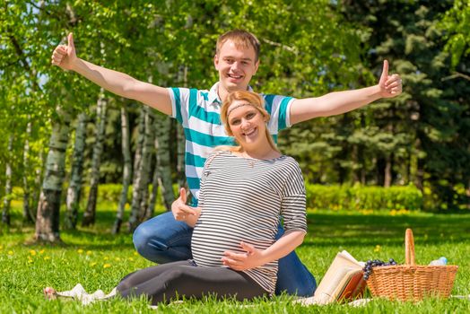 Happy pregnant couple showing thumbs up gesture with hands