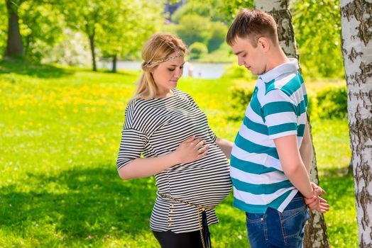 man and pregnant woman compare their stomachs, shot in the park summer day