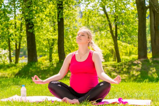 happy pregnant woman in a lotus position doing yoga in the park