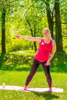 young pregnant woman doing exercises with dumbbells in the park