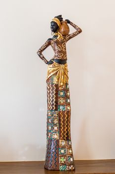 Africa figurine girl standing on a wooden table on a background of a white wall