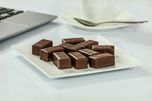 Chocolates on a plate next to a cup of coffee and laptop in the office