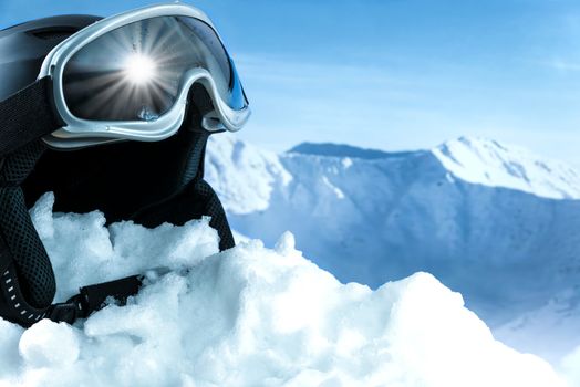 Helmet and ski goggles on snow with a blue sky and mountains