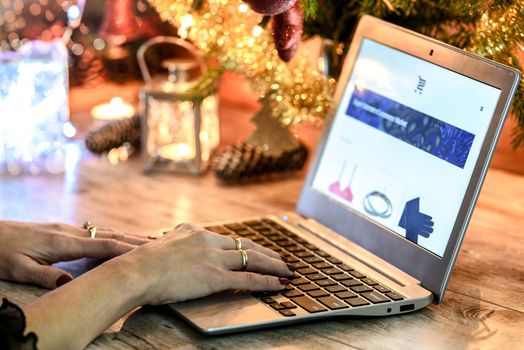 Woman doing Christmas e-shopping via laptop on the background of Christmas decorations