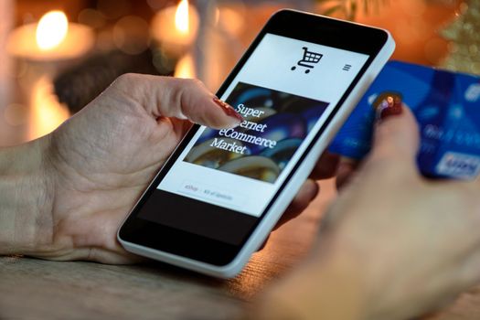 Woman makes shopping via smartphone and a credit card in the e-store on the bacground of candles