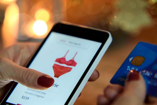 Woman purchasing red erotic lingerie via a smartphone application and a credit card