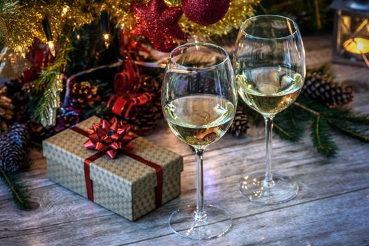 Two wineglas with white wine on a wooden table in the background of Christmas tree, gift and candles